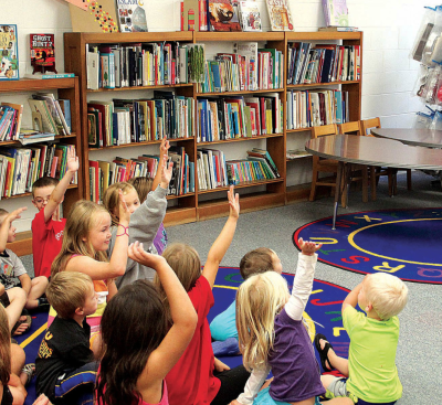 Children sitting on floor and raising hands in library